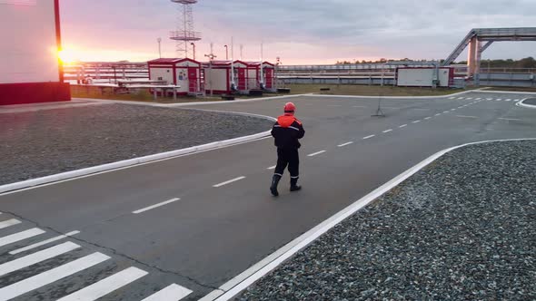 At Sunset an Employee in Overalls is Walking on the Territory of an Industrial Zone