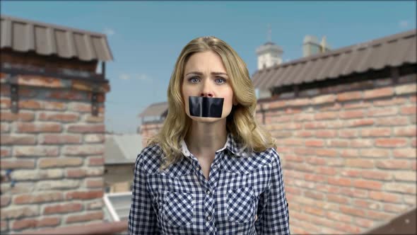 Expressive Young Woman with Taped Mouth Trying to Speak