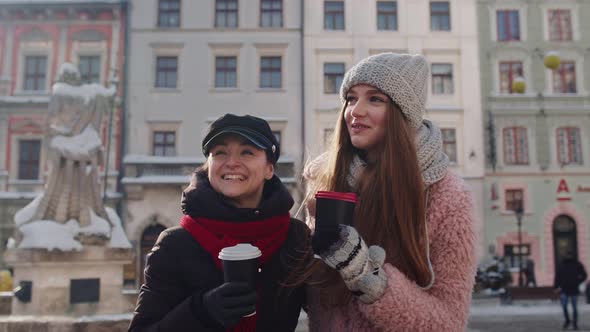 Two Smiling Women Tourists Traveling Together Drinking Hot Tea Coffee From Cups on City Street