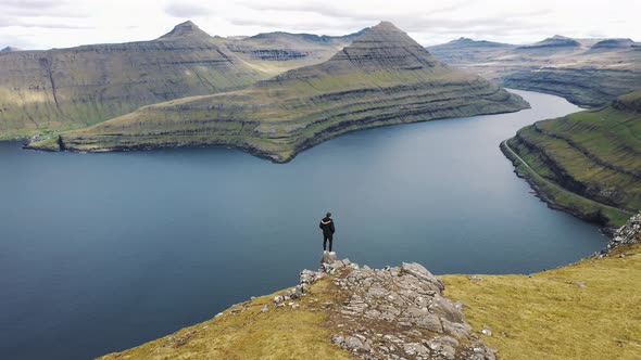 Flying Around a Hiker at the Top of a Mountain Above Funningur on Faroe Islands