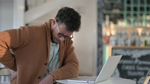 African Man Having Back Pain While Using Laptop Cafe