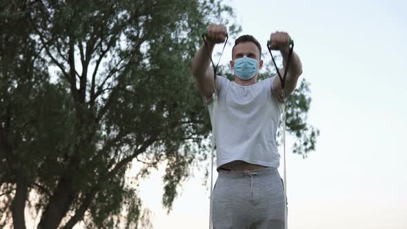The athlete performs exercises with the help of an expander on the street in quarantine.