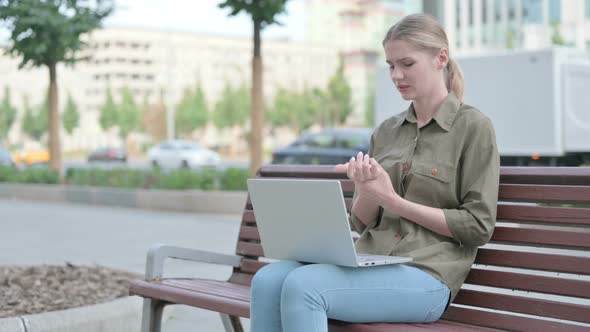 Woman with Wrist Pain Using Laptop while Sitting Outdoor on Bench