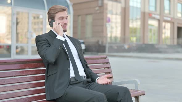 Businessman Talking on Phone While Sitting Outdoor on Bench