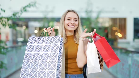 Portrait happy young cheerful woman showing shopping in gift paper bags looking at camera 