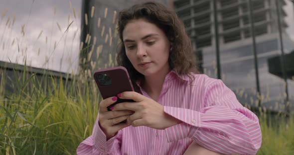 Cheerful female tourist using navigator on modern phone device sitting on urban streets