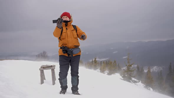 Man Blogger Takes a Photo on the Top of the Mountain in Heavy Snowy Weather