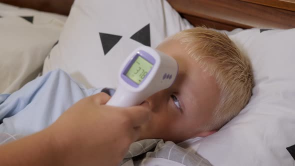 A Mother Measures the Temperature of a Sick Boy with an Infrared Thermometer