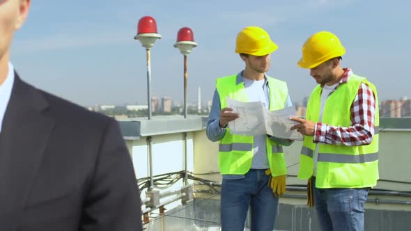 Responsible Male Engineer in Safety Helmet Looking at Cam Builders on Background