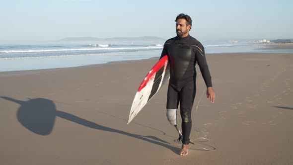 Long Shot of Serious Surfer with Disability Walking Along Shore