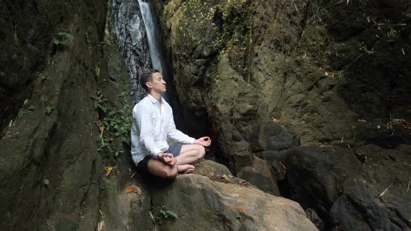 Handsome Young Man Meditates on Rock in Yoga Lotus Position