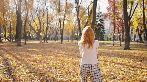 Young Happy Woman Having Fun Throwing Leaves and Dancing Under Golden Rain Enjoying Walk in Autumn