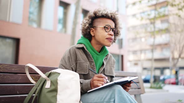 Confident African woman wearing green hoodie writing notes in notepad
