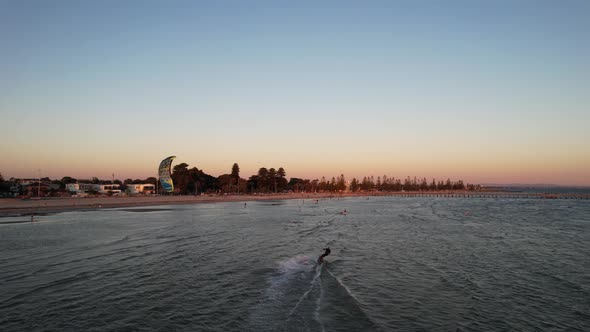 Drone following kite surfer from behind on a flat ocean as the sunsets.