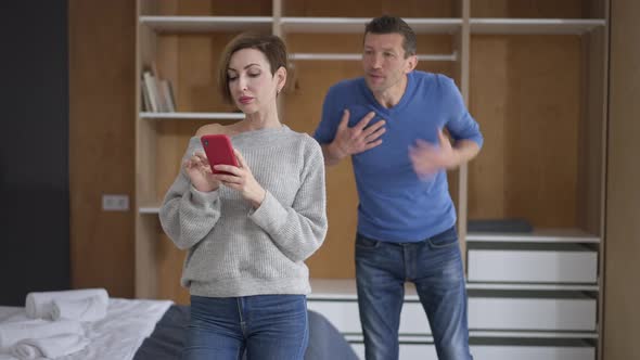 Absorbed Wife Surfing Social Media on Smartphone Ignoring Husband Gesturing Shouting at Background