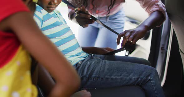 Animation of happy african american mother fastening belts in children seats in car