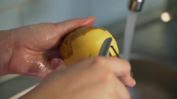 Woman Peels Ripe New Potatoes with Vegetable Peeler Over Silver Sink Near the Flowing Water in the