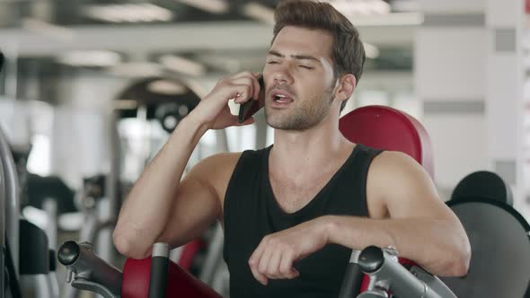 Athlete Man Talking Smartphone After Training on Sport Machine in Fitness Gym