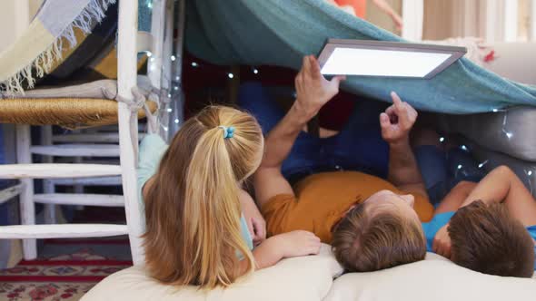 Caucasian father, son and daughter lying in house of blankets using tablet copy space on screen