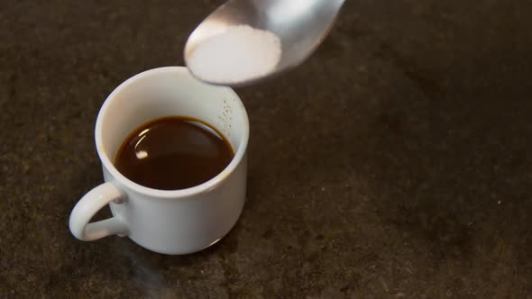 Sugar being added to coffee with metal spoon, close up