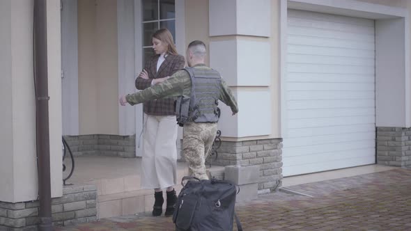 The Man in Military Closes with a Bag Comes Back Home and Meets His Wife in Front of House. The Lady