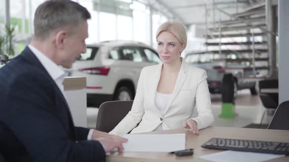 Portrait of Young Caucasian Blond Woman in Elegant Suit Receiving Papers From Car Dealer and Signing