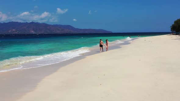 Two people engaged on exotic coastline beach voyage by transparent sea with white sand background of