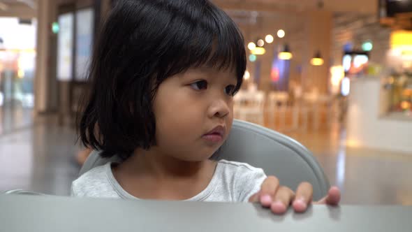 a little asian girl sitting in food court with father for waiting her mom buy some meal for lunch