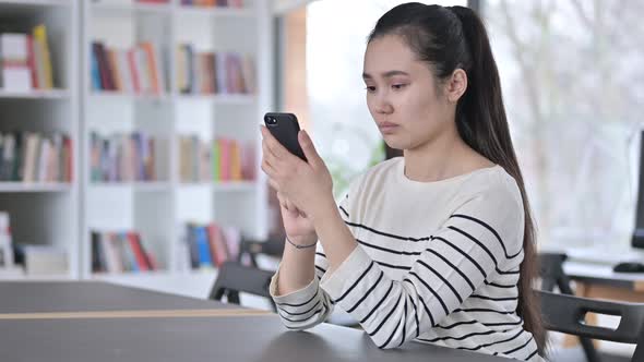 Serious Young Asian Woman Using Smartphone in Library 