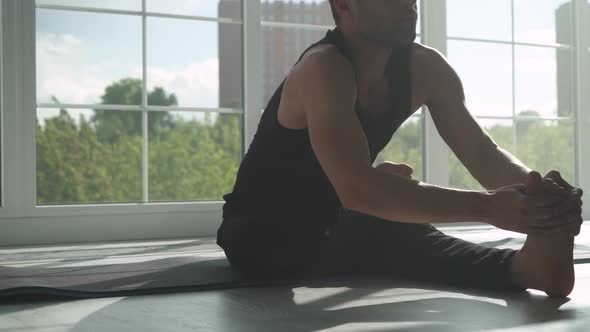 Young Man Doing Yoga in a White Room Filled with Light the Man Does Stretching of the Muscles Near