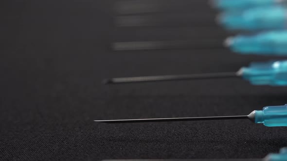 A Lot of Needles on Syringes Lie on Black Table. A Macro Footage Camera Flow Past Sharp Medical