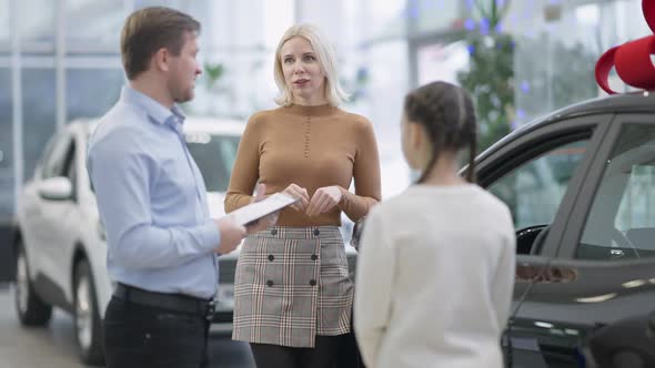 Portrait of Confident Blond Woman Talking with Car Dealer Choosing New Vehicle with Daughter