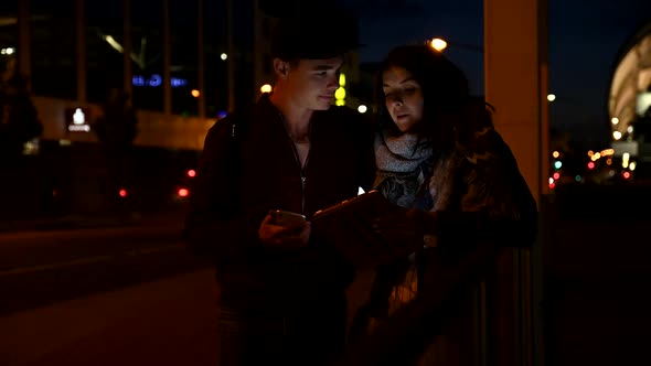 Couple using tablet and smartphone on the street at night