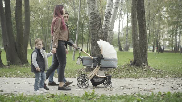Side View of Relaxed Young Family Strolling in Spring or Summer Park and Talking
