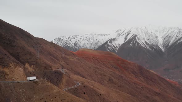 Aerial of View of a Road on Mountain Pass with Large White Truck Passing Through It Against