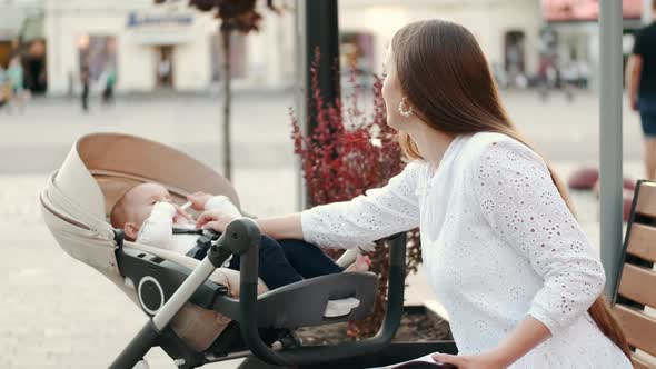 Mother Sitting on Banch with a Baby in Pram and Read Papers