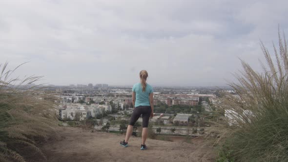 A young woman runner standing at the top of trail overlooking neighborhood.