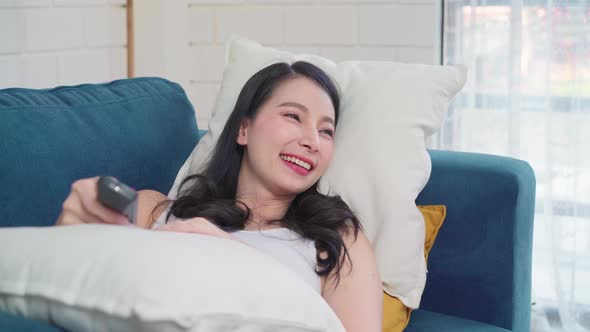 Young Asian woman watching TV at home, female feeling happy lying on sofa in living room.
