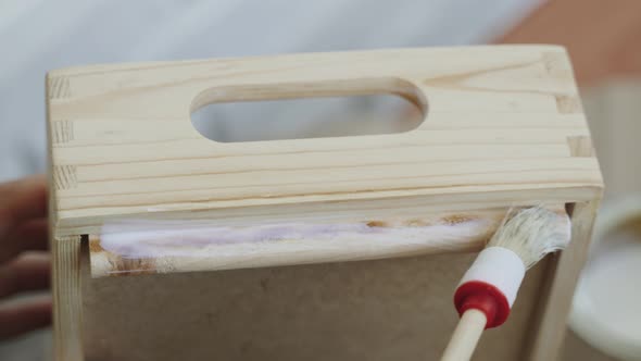 Brush Applies White Liquid to Legs and Handles of Wooden Box Closeup