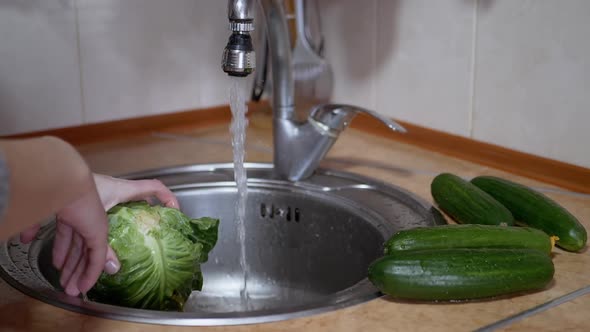 Female Washing Green Cabbage Cucumbers with Running Water From a Tap in Kitchen
