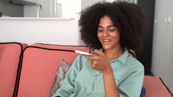 Smiling Africanamerican Woman with Curly Hair Holding Phone and Speaking on Speakerphone