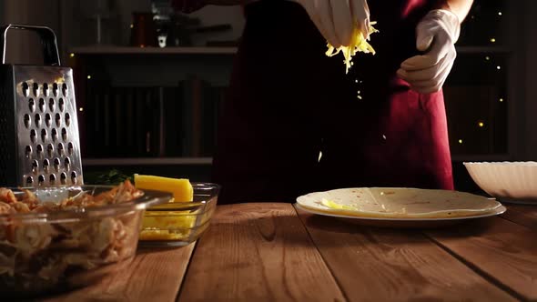 Cook Hands in Gloves Throwing Grated Cheese on Tortilla Lying on Plate on a Wooden Table in Slowmo