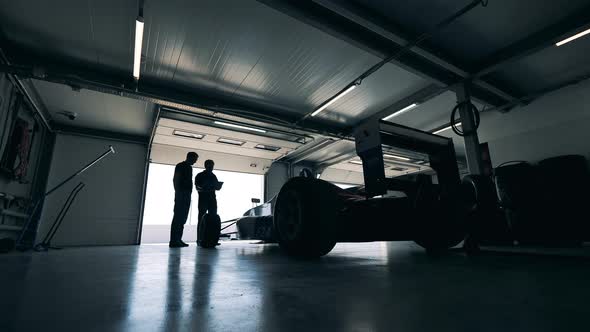 Garage with Two Men Talking While Observing a Racing Car
