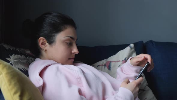 Asian woman using smartphone while lying on home sofa in her living room. Happy female use phone