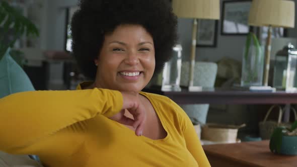 Video of happy plus size african american woman sitting on sofa