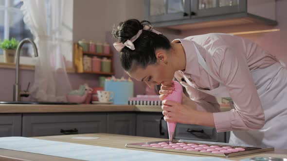 Pastry Chef in Apron Piping Out Dough Mixture for Pink Macarons Shells on Slip Mat on Backing Tray