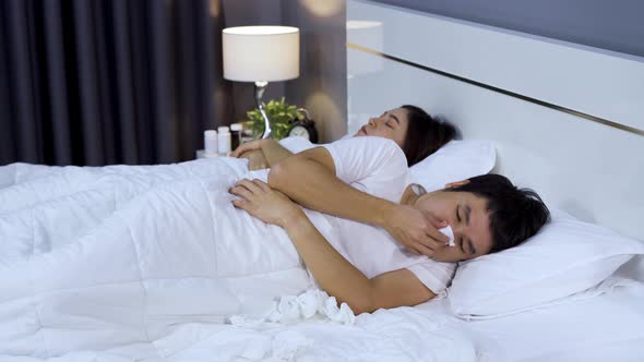 sick man sneezing while his wife is sleeping on bed at home