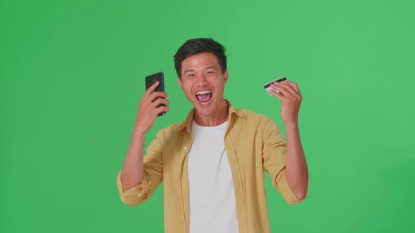 Asian Man Using Mobile Phone With Credit Card And Celebrating In The Green Screen Studio