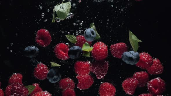 Fresh Raspberries with Blueberries and Fresh Mint Leaves Fall on a Black Background Into the Water