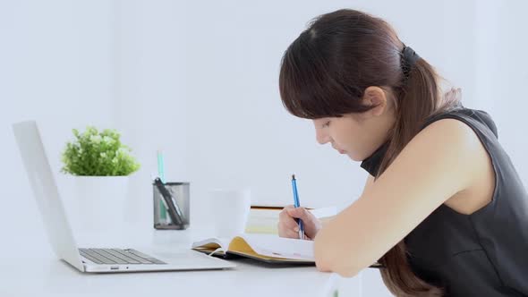 Young asian woman smiling sitting in the living room study and learning writing notebook and diary.
